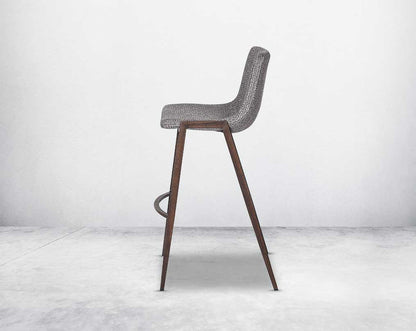 this wooden bar stool is a striking mix of industrial and modern. The supple seat, upholstered in fabric sits atop a stainless steel base in wood finish.