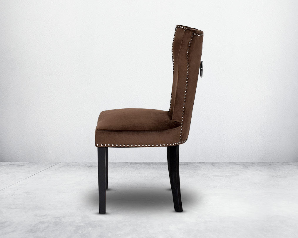 Dining chair upholstered in fabric with legs in wood. Stainless steel decorative ring at the back with stainless steel rivets.