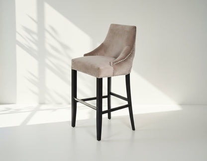 Bar chair upholstered in fabric with buttoned tufted back and silver rivets, the stool has a stainless steel front bar as a foot rest with legs in dark vintage brown wood 