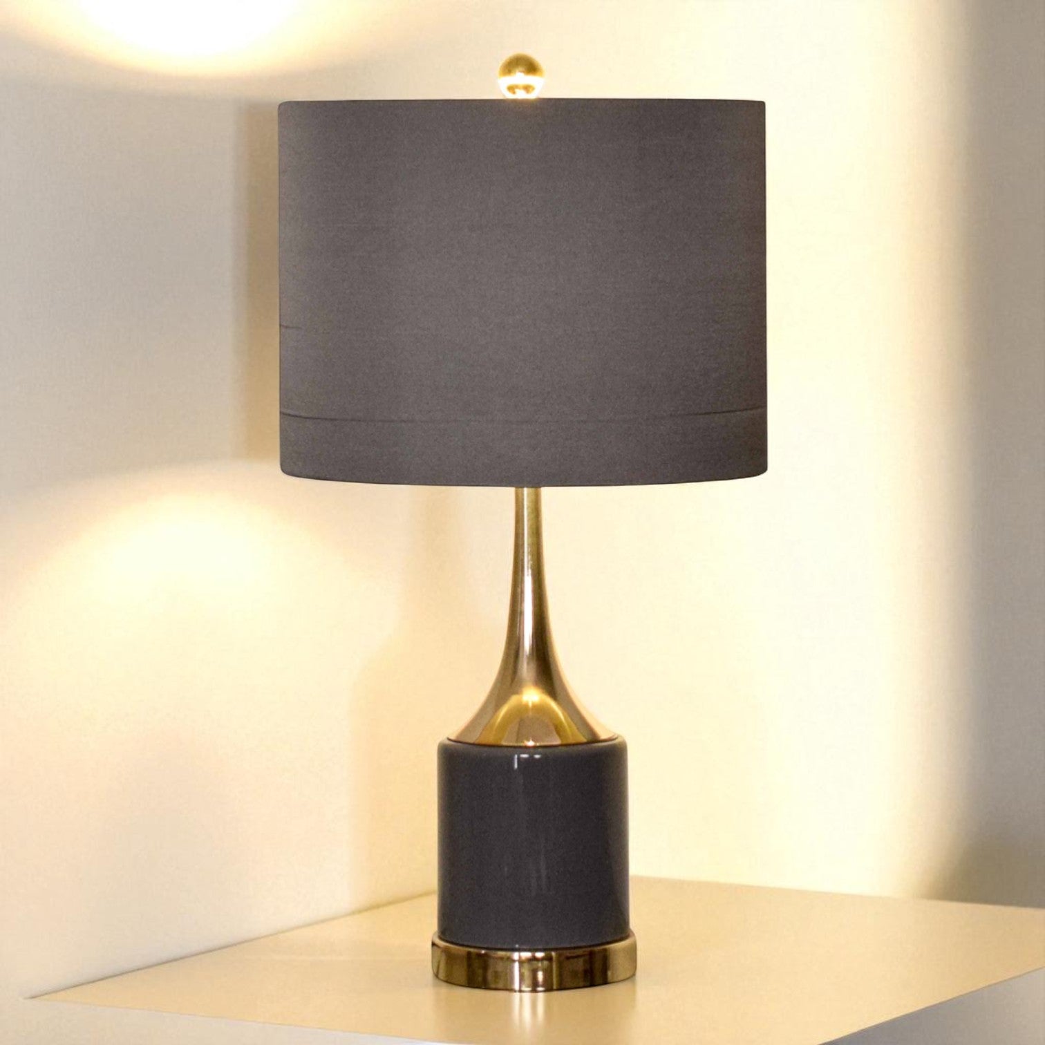 Table lamp with a dark gray shade and black base with gold accents on a light surface.