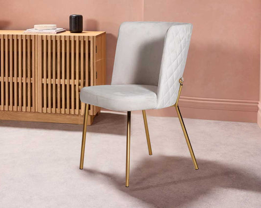 Minimalistically designed chair with criss-cross stitch padded fabric in gold finish stainless steel legs in contemporary design.